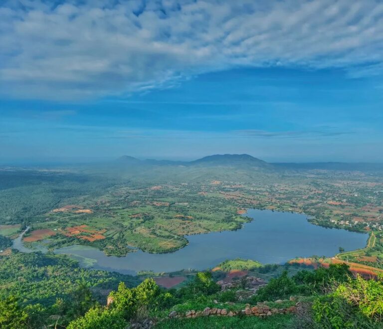 A serene sunrise over Makalidurga, illuminating the rocky terrain and dense vegetation below