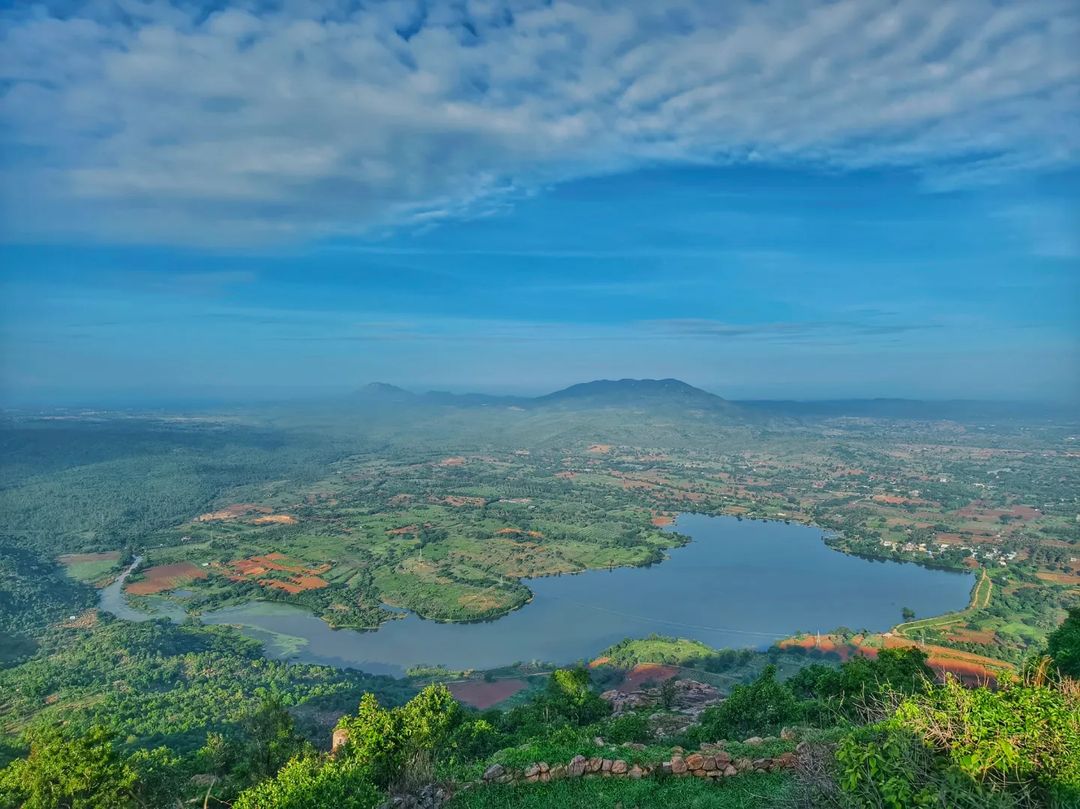 A serene sunrise over Makalidurga, illuminating the rocky terrain and dense vegetation below