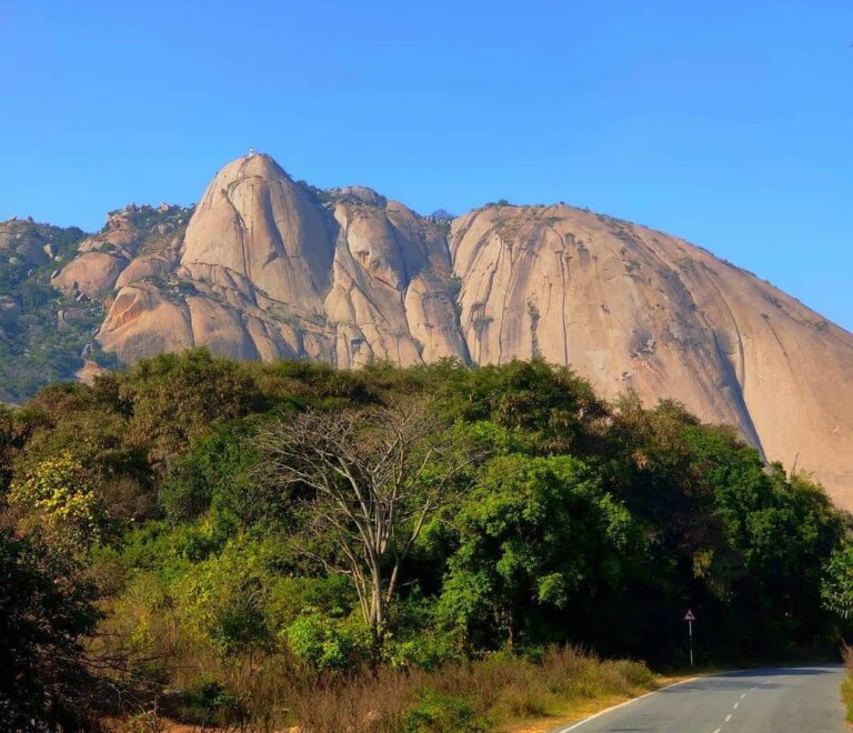 Scenic view of Savandurga Hill, a towering monolithic rock formation near Bangalore, India, surrounded by lush greenery and popular for trekking adventures.