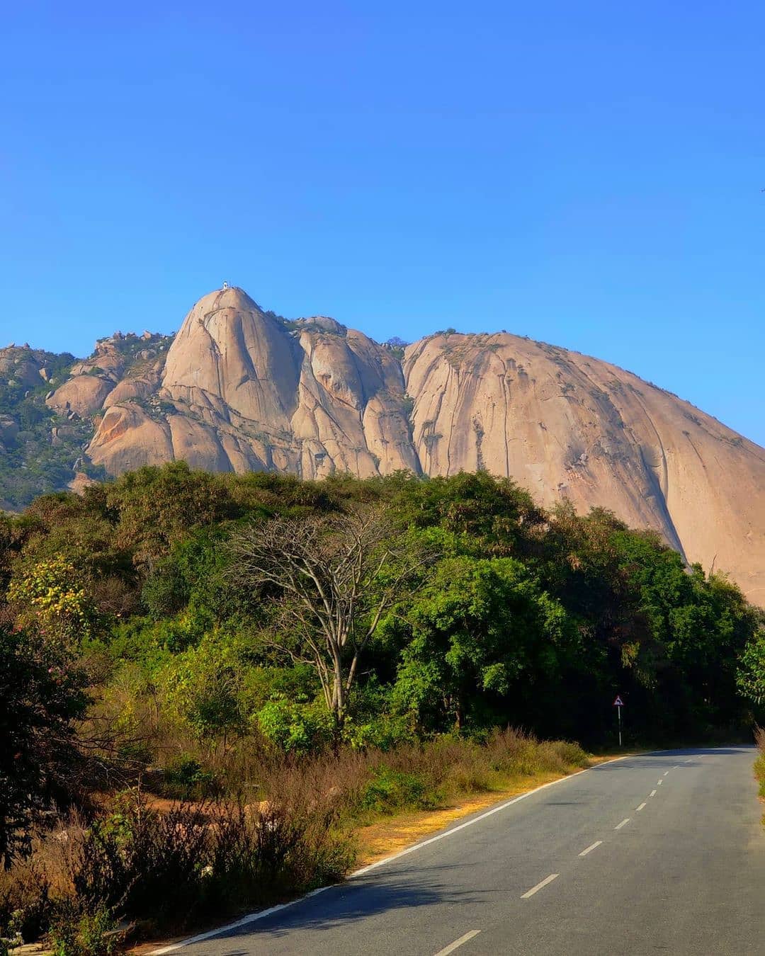 Scenic view of Savandurga Hill, a towering monolithic rock formation near Bangalore, India, surrounded by lush greenery and popular for trekking adventures.